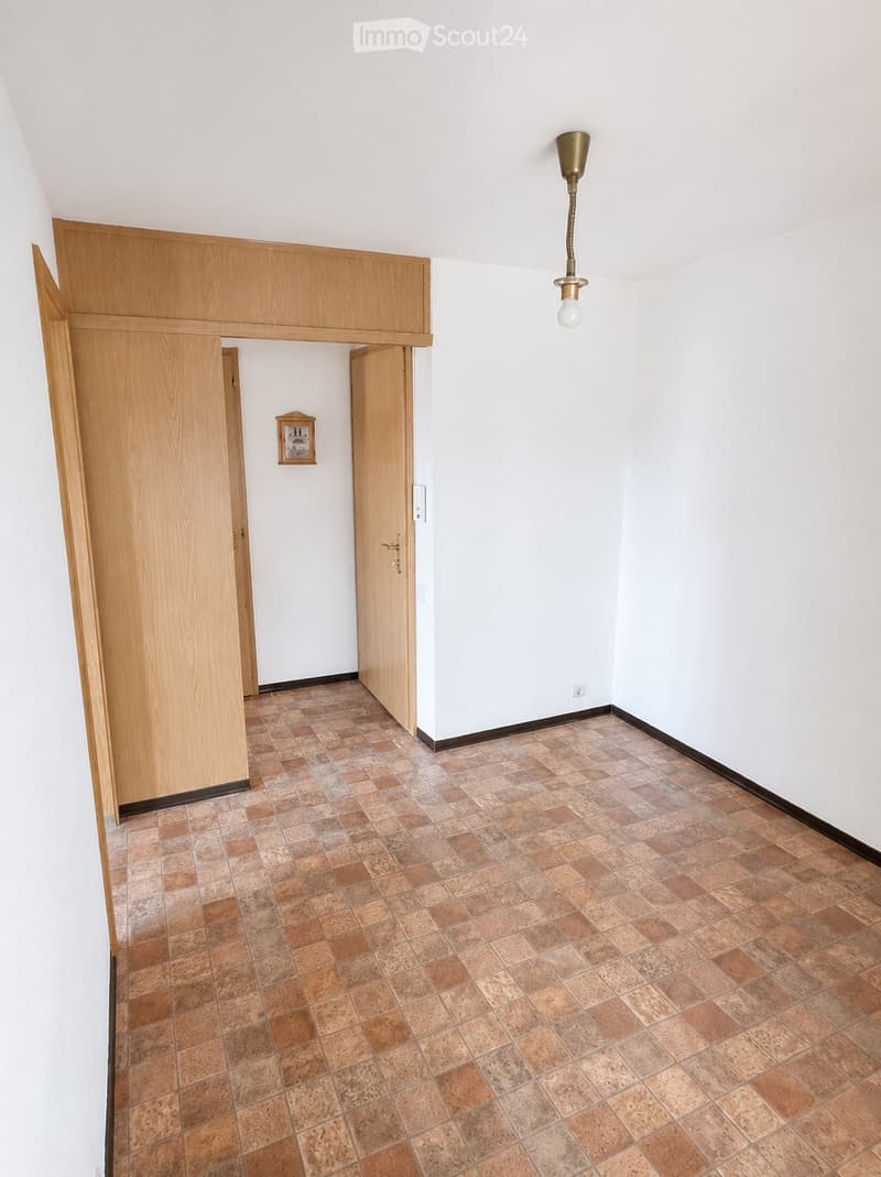 Empty hallway with tiled floor, white walls, wooden doors, and a small framed picture on the wall.