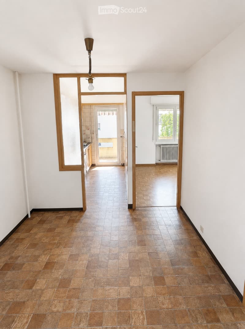 Empty hallway with tiled flooring, white walls, and wooden-framed doorways leading to other rooms.