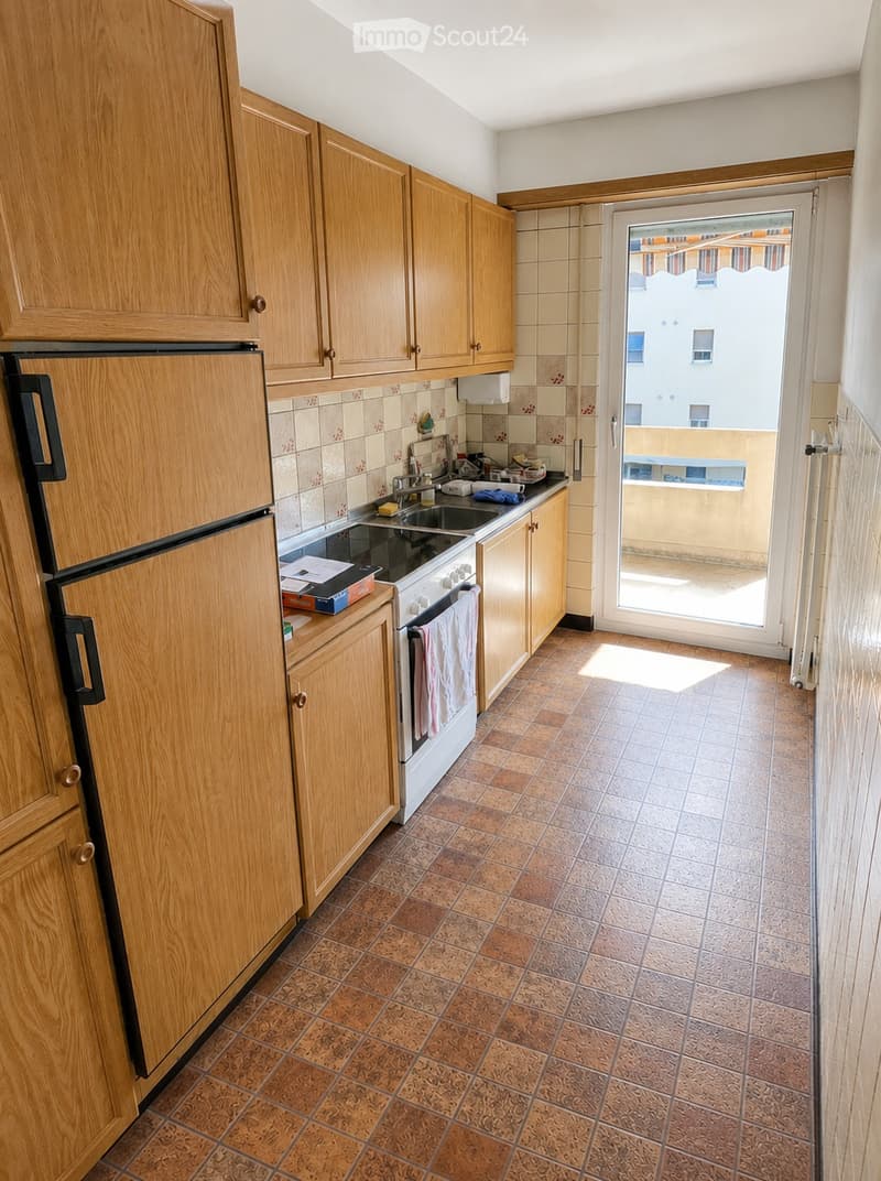 Kitchen with wooden cabinets, tiled floor, refrigerator, oven, sink, and a sliding door leading to a balcony.