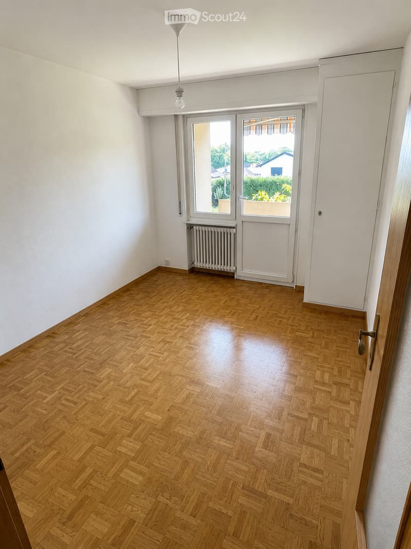 Empty room with wooden herringbone flooring, white walls, a radiator, a pendant light fixture, and a large glass door leading to a balcony or outdoor area.
