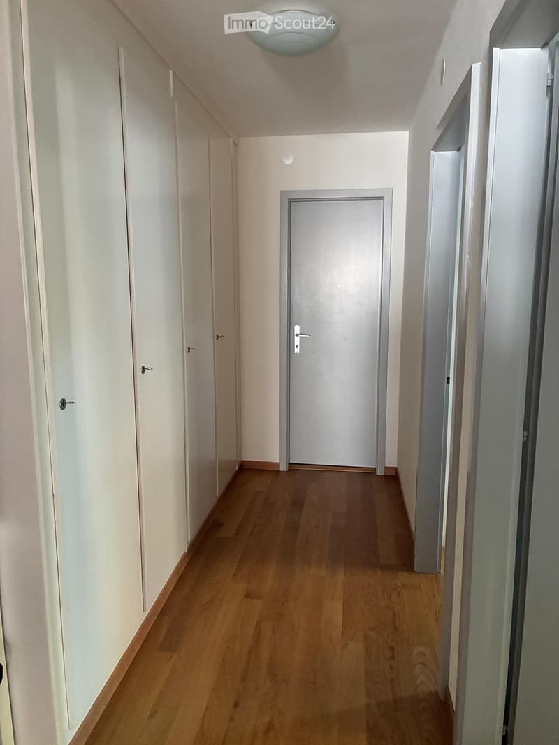 A narrow hallway with wooden flooring, white walls, and several closed doors on both sides.
