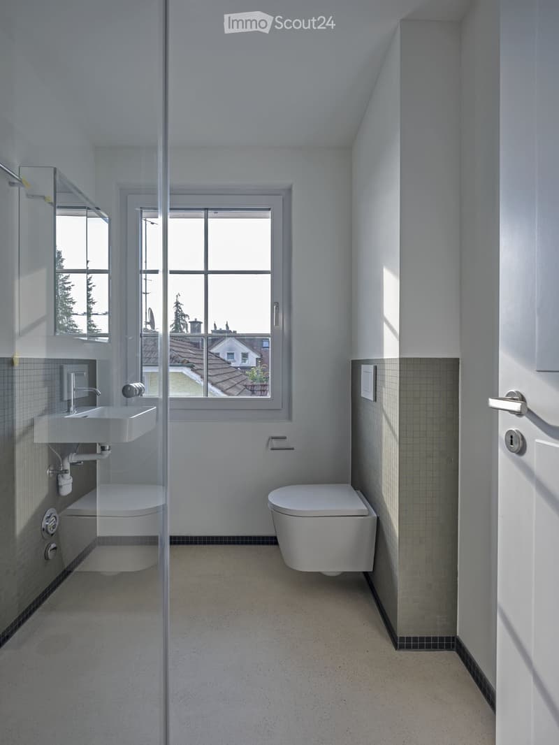 Modern bathroom with white walls, a large window, a sink, a toilet, and a glass shower enclosure.