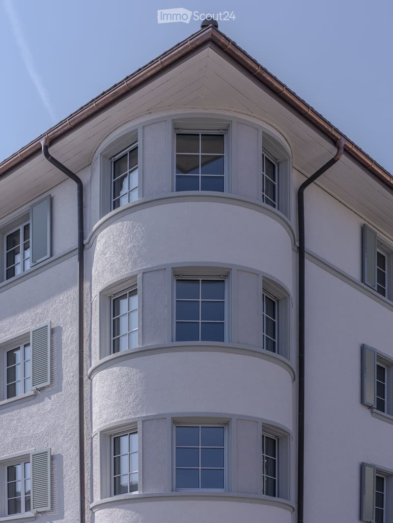 A multi-story building with white walls, multiple windows, and decorative architectural details including a curved section and a small dome on the roof.