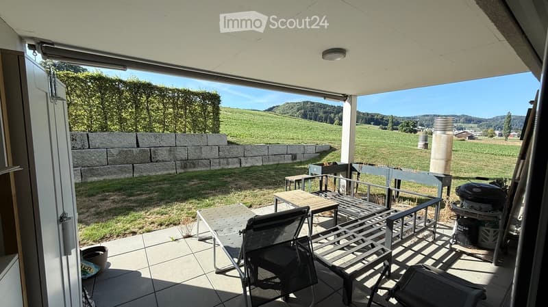 Balcony with outdoor furniture, overlooking a scenic countryside with hills and fields.