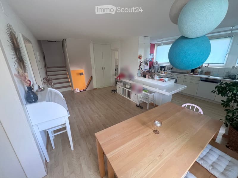 Open-plan living and dining area with wooden flooring, white kitchen island, dining table, chairs, and a staircase leading to another level.