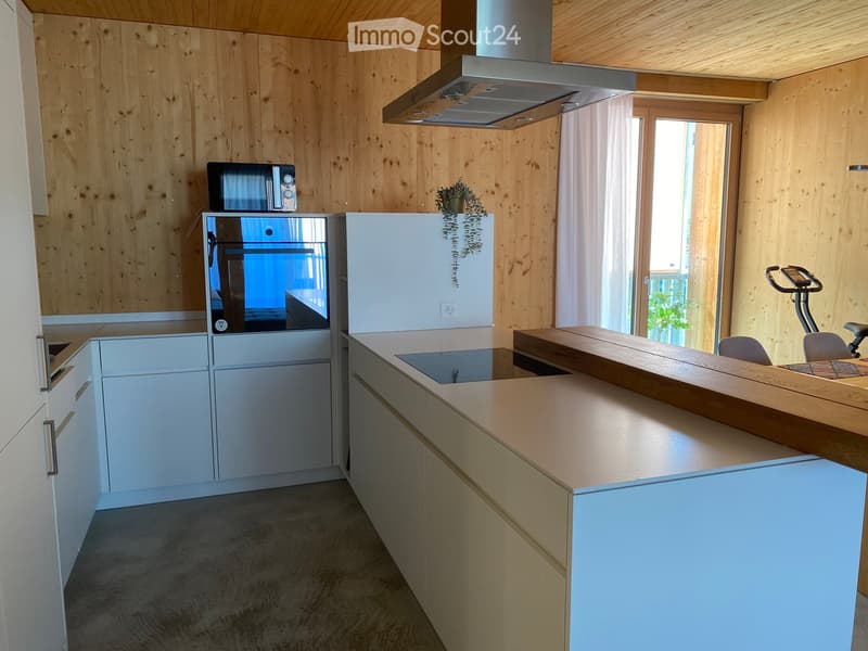 Modern kitchen with light wood walls, white cabinets, stainless steel appliances, and a wooden kitchen island. An exercise bike is positioned near the window.