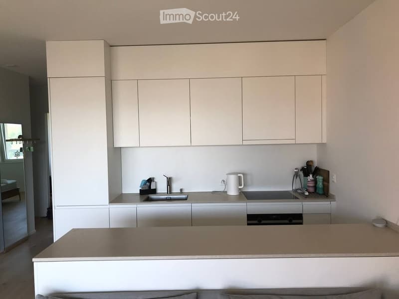 Modern kitchen with white cabinets, a central island, and various appliances including a sink, oven, and countertop items.