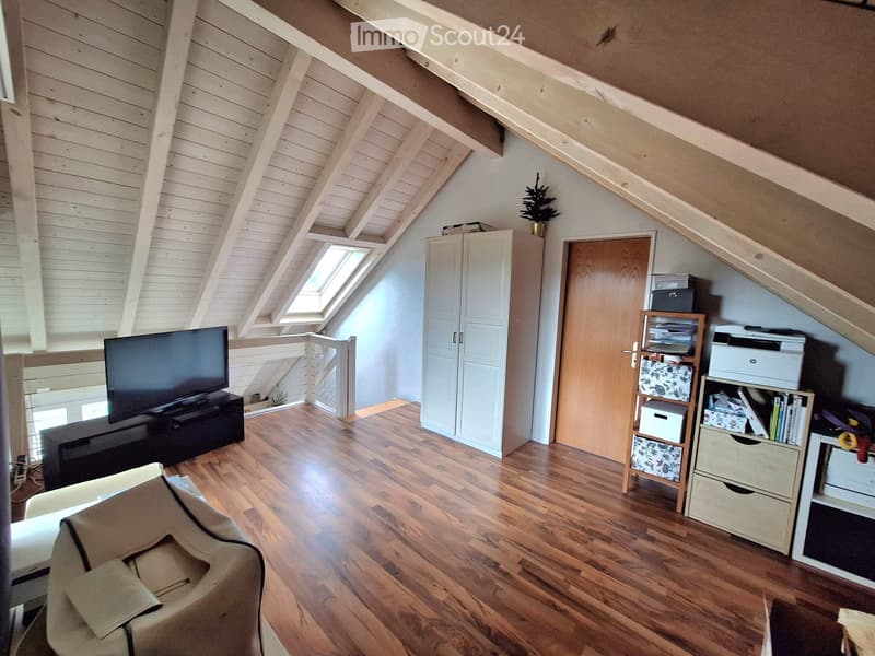Bright attic room with wooden floors, slanted wooden ceiling, large skylight window, and modern furniture including a sofa, TV, and storage units.