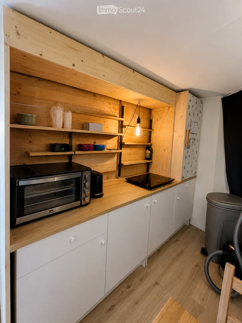 Modern kitchen with wooden shelves, white cabinets, and stainless steel appliances including an oven and refrigerator. Wooden countertop and flooring.