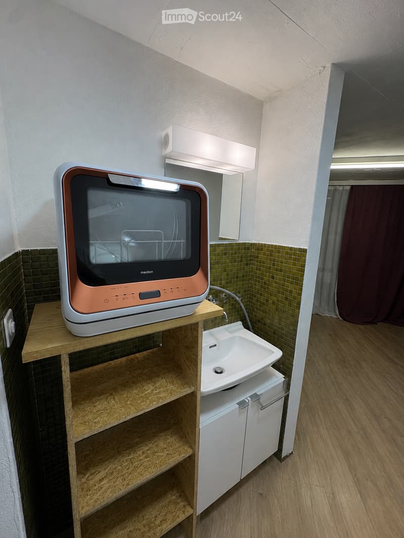 Bathroom with a wooden shelf holding a microwave, a white sink with a cabinet underneath, and a mirror above the sink.