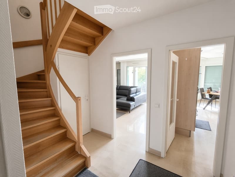 Bright hallway with wooden staircase, open doors leading to living and dining areas, modern interior design.
