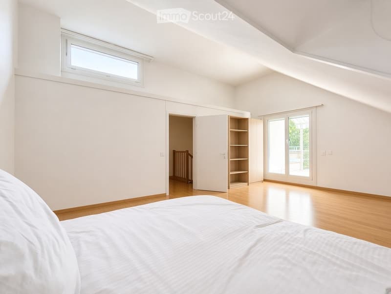 Bright bedroom with wooden flooring, white walls, large window, sliding glass door leading to a balcony, and a built-in wardrobe with shelves.
