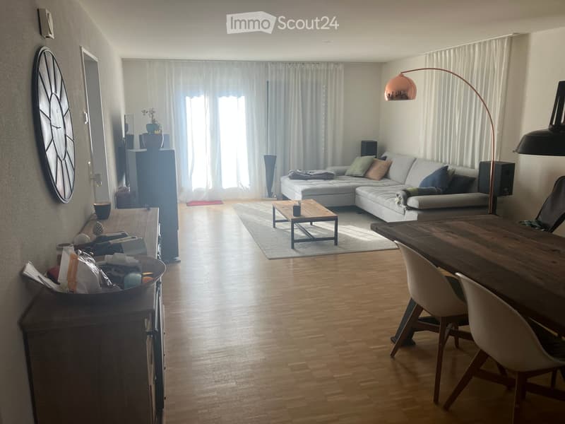 Furnished Room. Bright living and dining area with wooden flooring, a grey sectional sofa, a coffee table, a dining table with chairs, and a floor lamp.