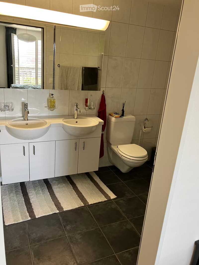 Bathroom. Modern bathroom with double sink vanity, large mirror, toilet, and tiled floor. Features include a striped bath mat, towel, and various toiletries.