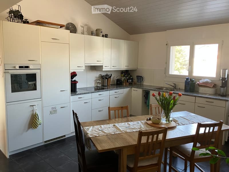 Kitchen. Bright kitchen with white cabinets, granite countertops, and a wooden dining table with chairs. Appliances include a refrigerator, oven, and dishwasher. A vase of tulips is on the table.