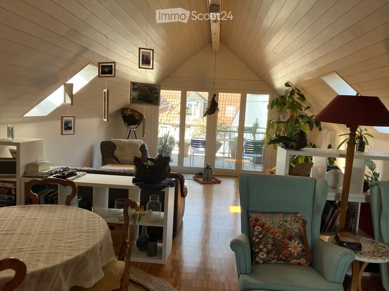 Furnished Room. Bright, airy room with wooden floors, large windows, and skylights. Features a green armchair, sofa, dining table, shelves, and decorative items.