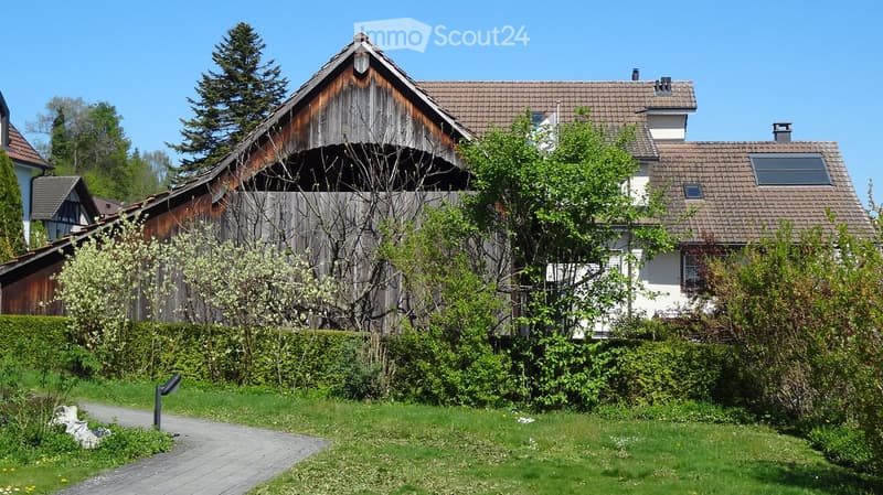 House. A two-story house with a traditional wooden barn attached, surrounded by greenery and a well-maintained lawn.