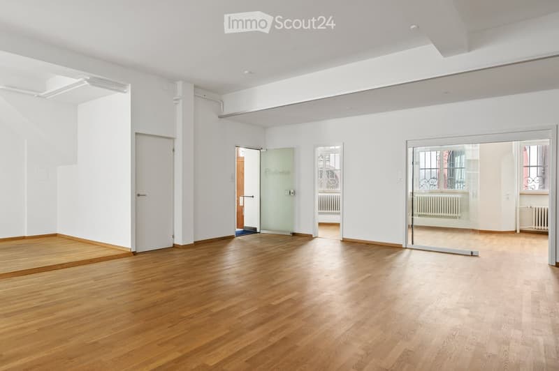 Empty room with wooden flooring, white walls, and multiple doors including a glass door leading to another space.