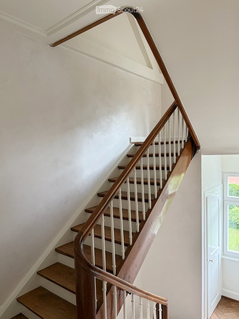 Spiral staircase with wooden steps and white balusters, leading upwards with a wooden handrail.