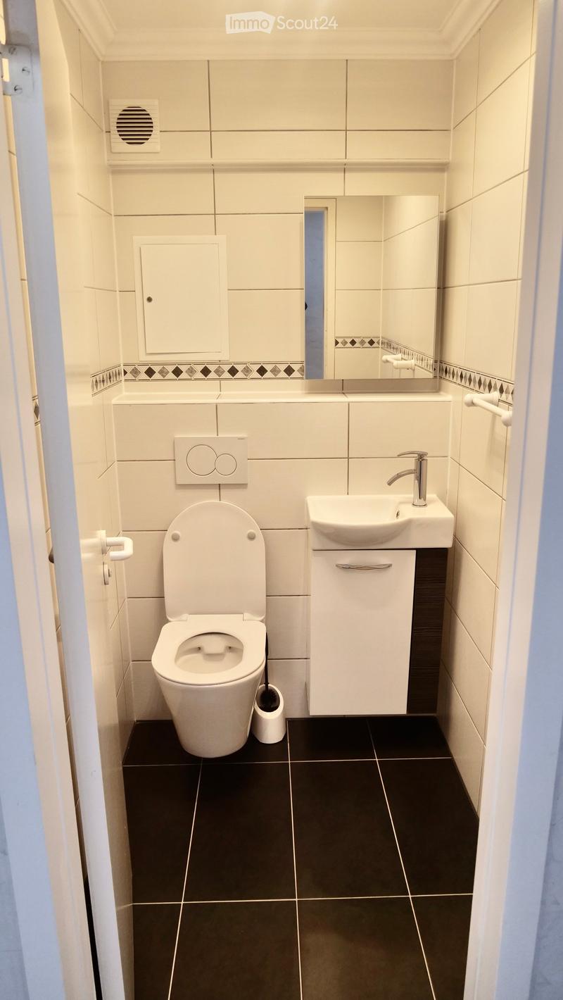 Modern bathroom with white tiles, black floor tiles, toilet, sink, mirror, and cabinet.