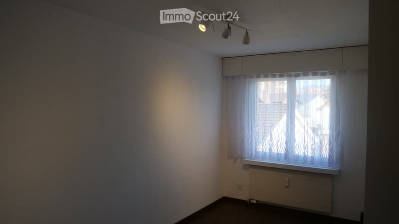 Empty room with white walls, a window with sheer curtains, a radiator, and a track light fixture on the ceiling.