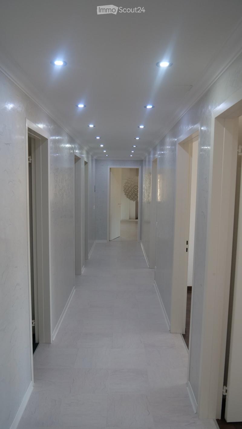 Clean, modern hallway with white marble walls and floor, recessed ceiling lights, and several open doors leading to other rooms.