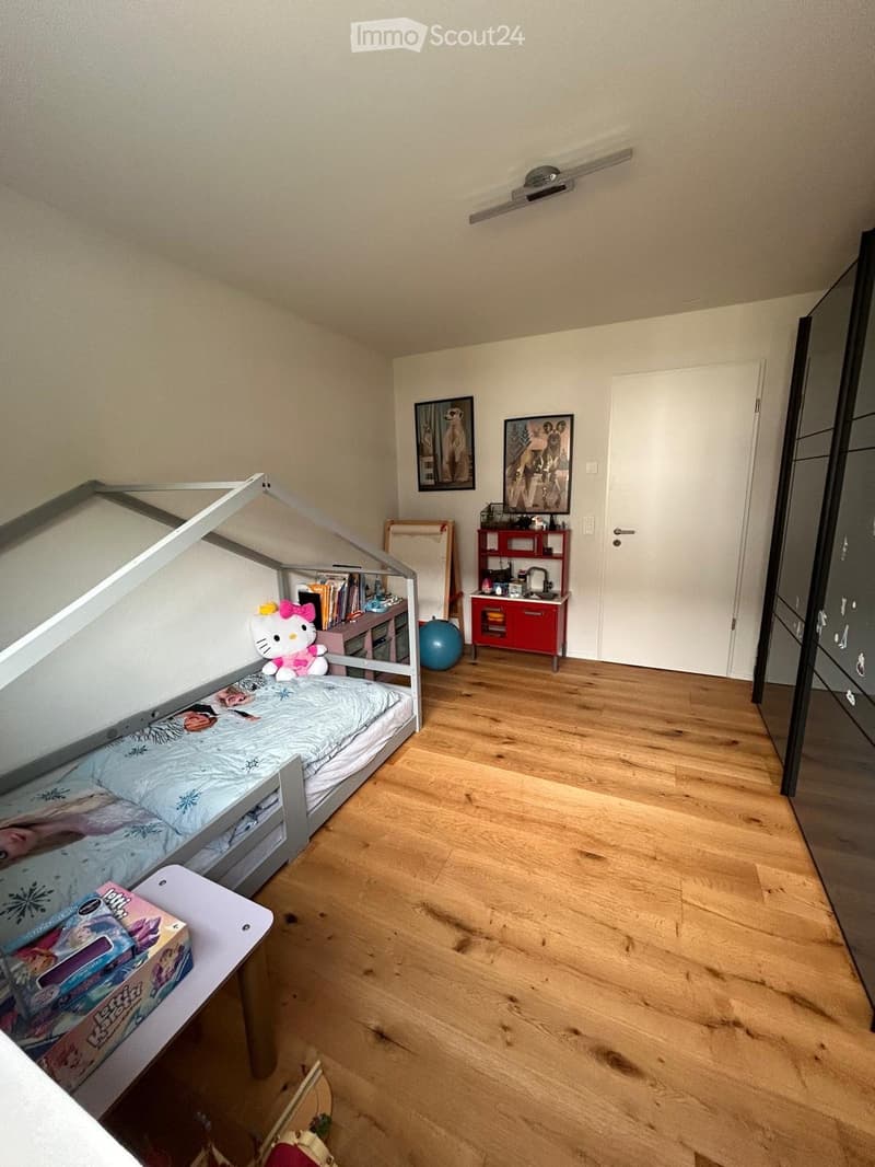 A child’s bedroom with a lofted twin-sized bed, a small table with a toy box, a red cabinet, a blue ball, and a Hello Kitty plush toy on the bed.