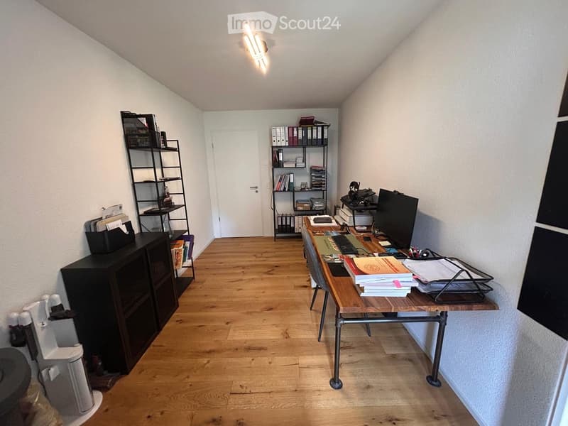 A well-organized office space with a wooden floor, a large desk with a computer setup, shelves filled with books and files, and a cabinet for storage.