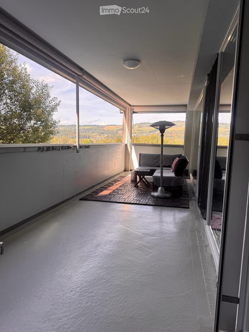 Balcony with a sofa, table, chair, and floor lamp, offering scenic views of the countryside.