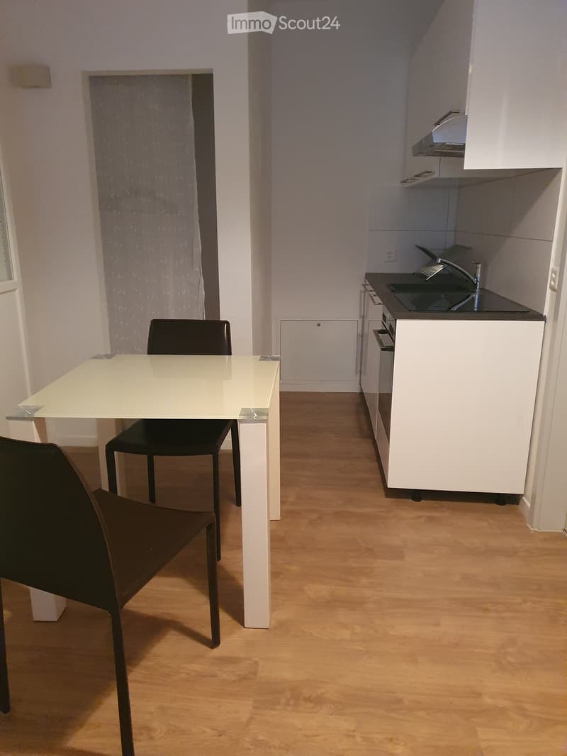 A modern, compact kitchen and dining area with white cabinets, a black countertop, a white dining table, and two black chairs.