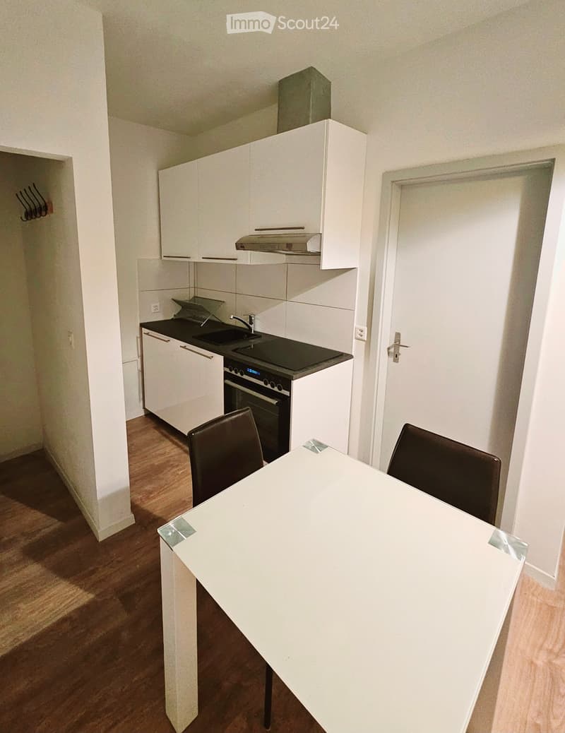 Modern kitchen with white cabinets, black countertop, built-in oven, sink, and a small dining area with a table and chairs.
