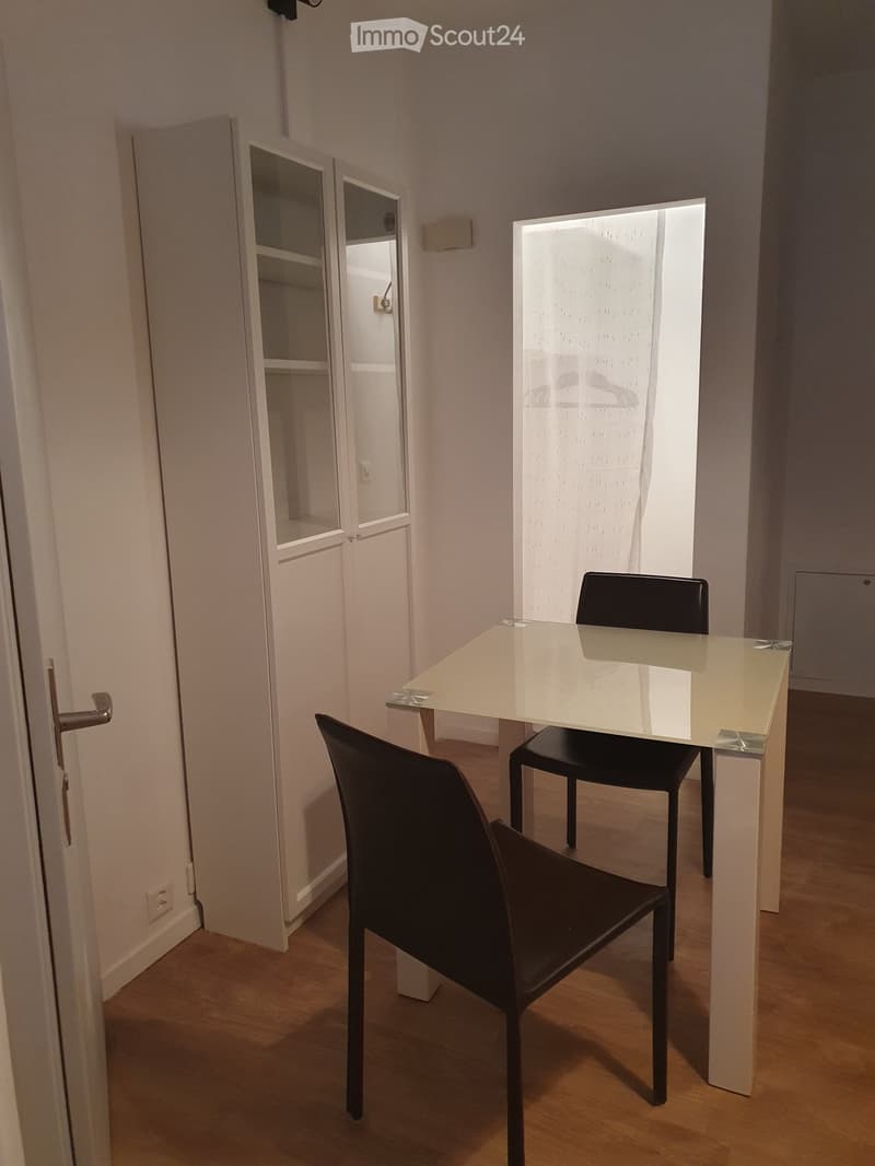 A small, modern dining area with a glass table and two black chairs, adjacent to a closet with mirrored doors.
