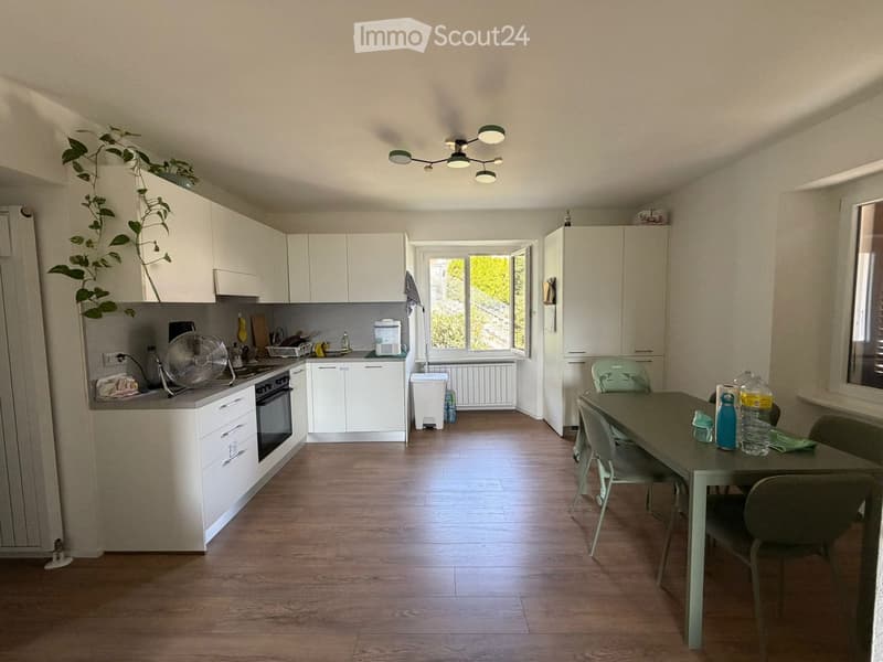 Bright kitchen with white cabinets, wooden flooring, and a dining area with a table and chairs. Includes an oven, fan, and various kitchen items.