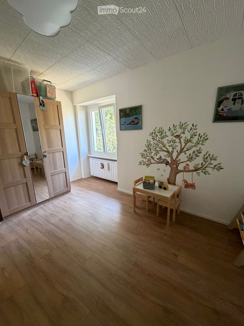 Child's room with wooden flooring, a small table and chairs, a mirror, a radiator, and a wall mural of a tree with animals.
