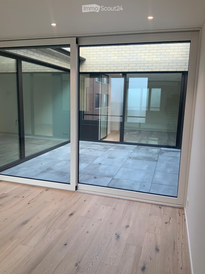 Empty room with light wooden flooring and large glass sliding doors leading to a tiled outdoor area.