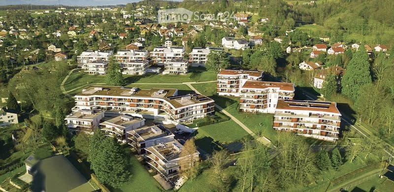 Aerial view of a residential area with multiple apartment buildings, surrounded by greenery and trees.