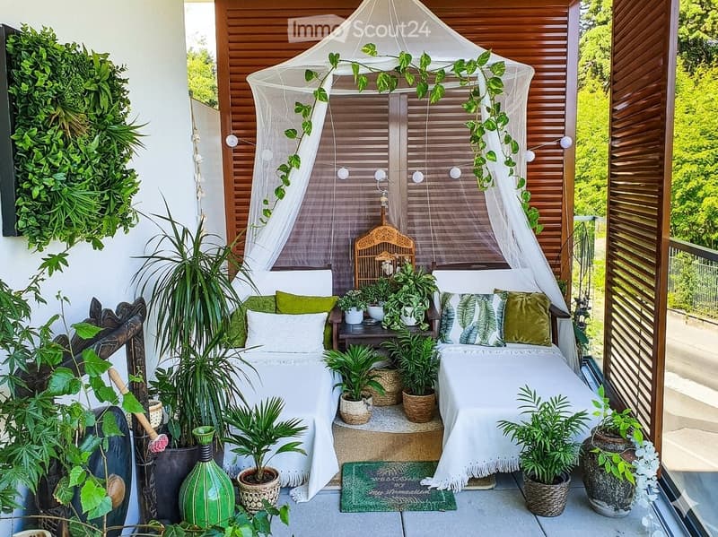 A cozy outdoor area with a white canopy bed, green cushions, potted plants, and decorative items.