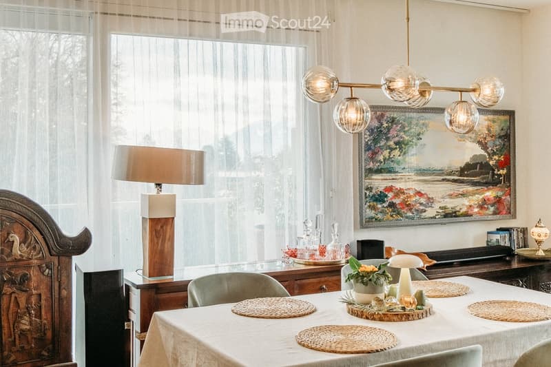 Dining room with a white tablecloth-covered table, six chairs, a floor lamp, a cabinet, and a painting on the wall.