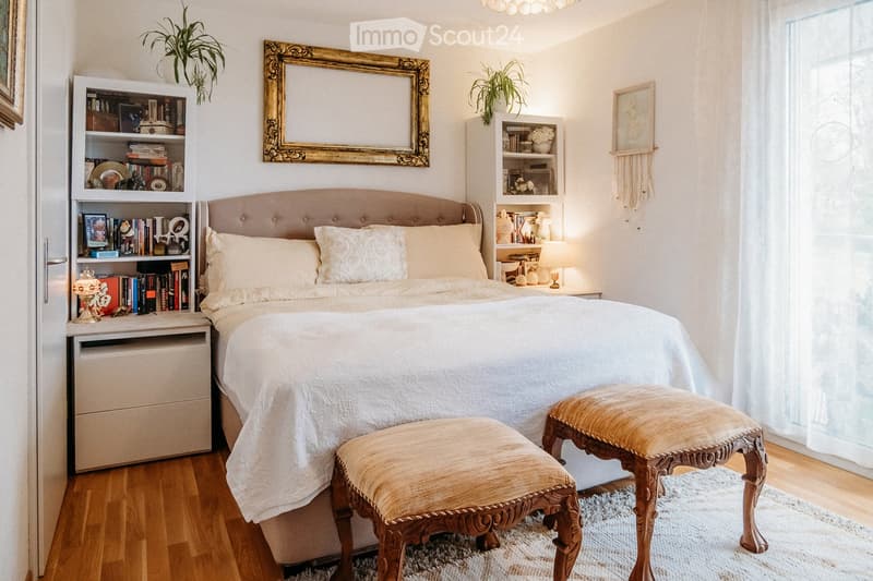 Cozy bedroom with a large bed, nightstands, two ornate stools, bookshelves, and decorative mirrors.
