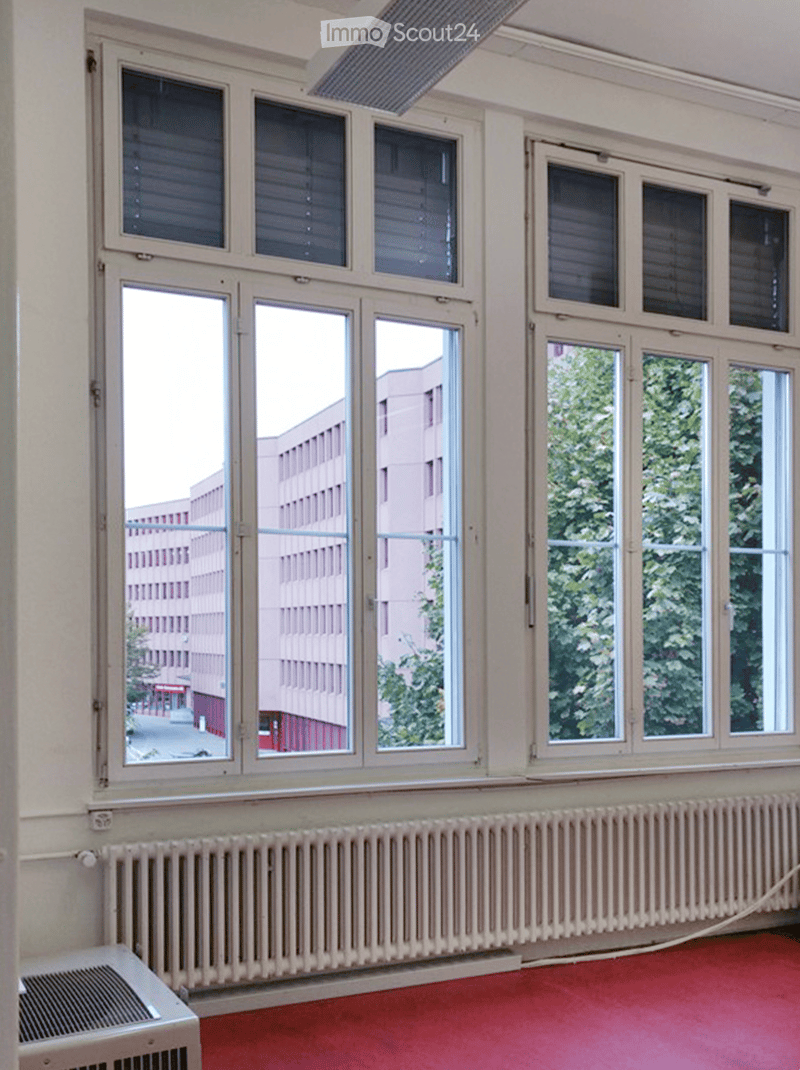 Empty room with large windows, radiators, and a red carpeted floor. No furniture or equipment is present.