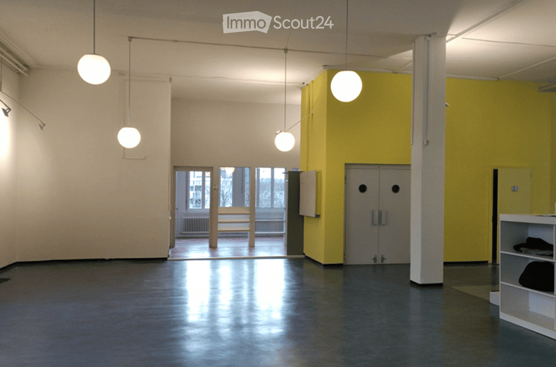Empty room with polished dark flooring, white walls, and modern lighting fixtures. Features include a large doorway leading to an outdoor area, a yellow accent wall, and a white shelving unit with a few items on it.