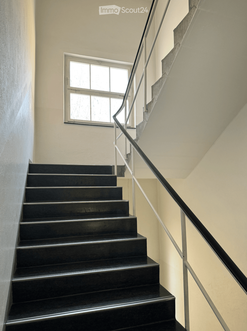 Modern staircase with dark wooden steps and metal railing, leading up to a windowed landing.