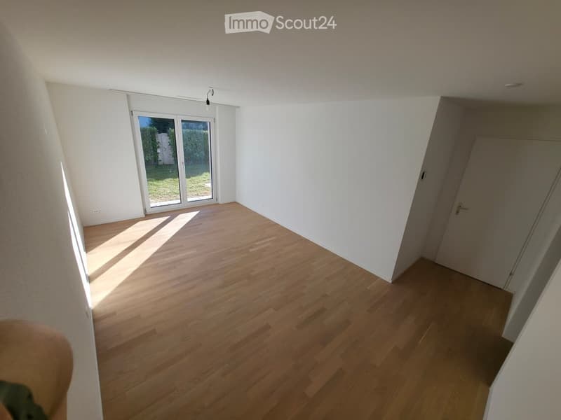 Empty room with wooden flooring, white walls, and large sliding glass doors leading to a garden area.