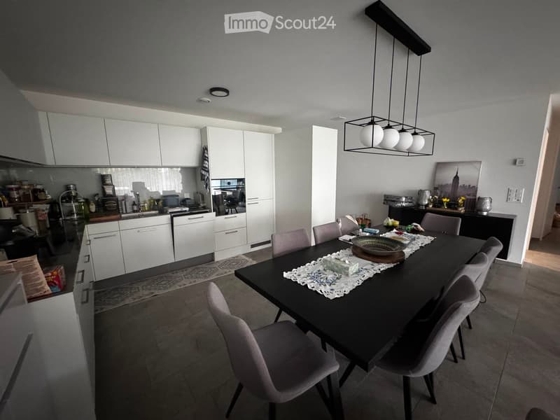 Modern kitchen and dining area with white cabinets, a black dining table with six chairs, and various kitchen appliances.