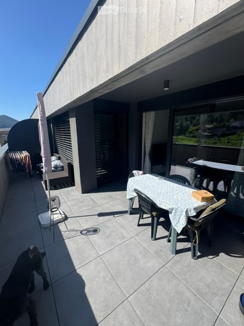 Balcony with tiled floor, outdoor dining table and chairs, umbrella, and scenic mountain view.
