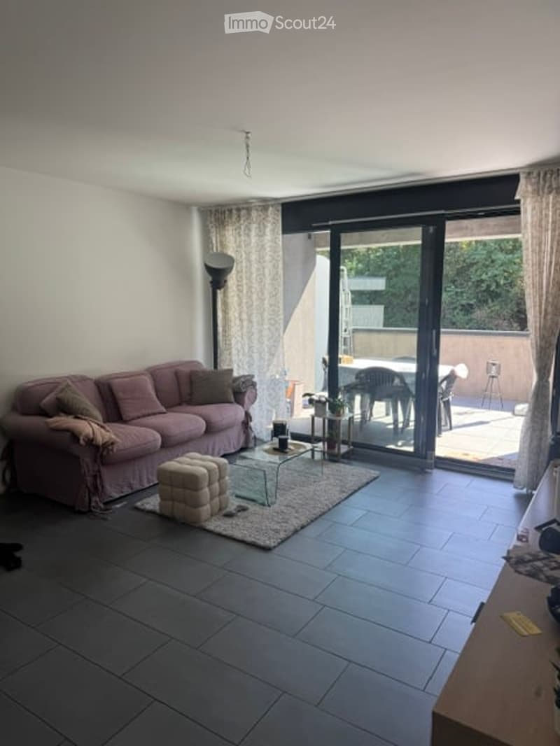 Modern living room with a pink sofa, ottoman, glass coffee table, side table, floor lamp, and access to a balcony with outdoor furniture.
