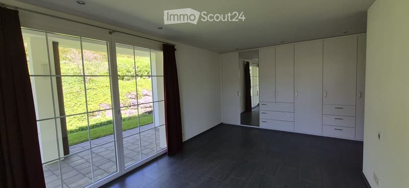 Empty room with large glass sliding doors leading to a garden, white built-in wardrobes, dark tiled floor, and neutral-colored walls.