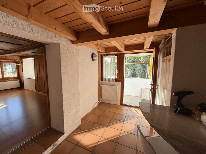 Empty room with wooden ceiling beams, tiled floor, and large windows. No furniture or equipment present.