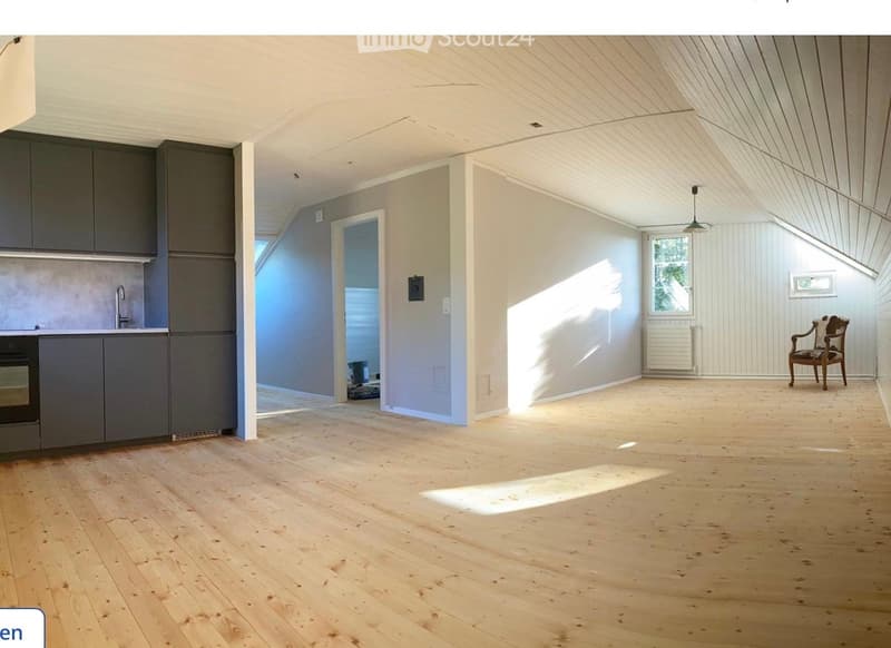 Bright, open room with wooden flooring, grey cabinets, and a single wooden chair near a window. Sunlight streams in, casting shadows on the floor.