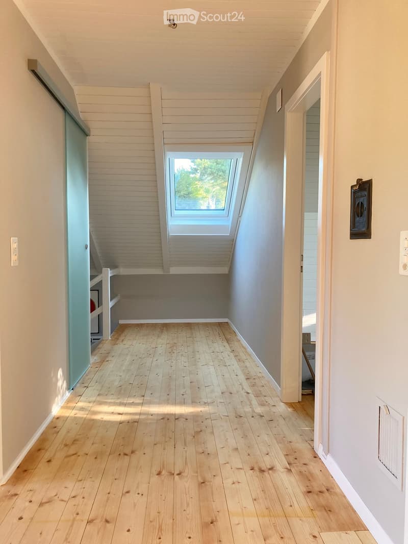 Bright hallway with wooden flooring, white walls, and a skylight window at the far end. Features a built-in shelf on the left and a door on the right.
